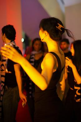Persoon die danst in geel podiumlicht, met anderen eromheen die drankjes vasthouden.