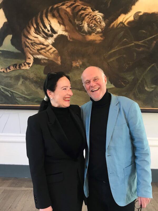 Hans Scholten and Trudy van Wielik stand smiling arm in arm in front of a large artwork featuring a tiger.