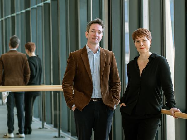 Emily Molnar, artistiek directeur van NDT, en Marc Pil, zakelijk directeur van NDT, poseren in een lichte dansstudio met glazen wanden.